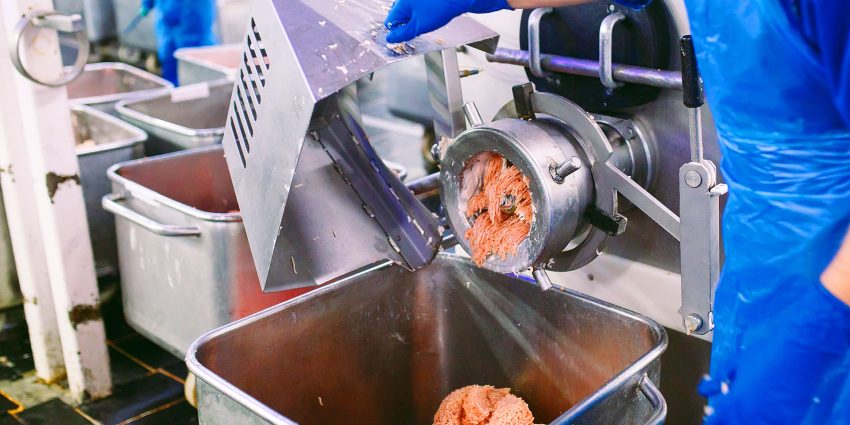 Meat processing worker operating industrial grinder machine in food production facility