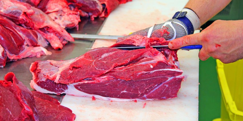 Butcher trimming fresh cut beef on processing table surface
